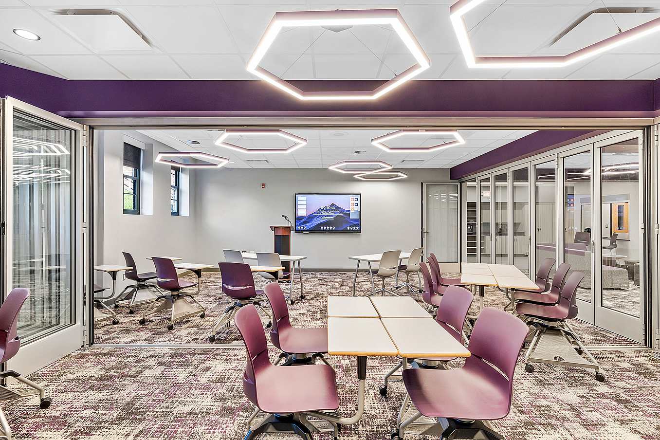A modern classroom featuring purple chairs, tables, and commercial glass doors fold to create a flexible space.