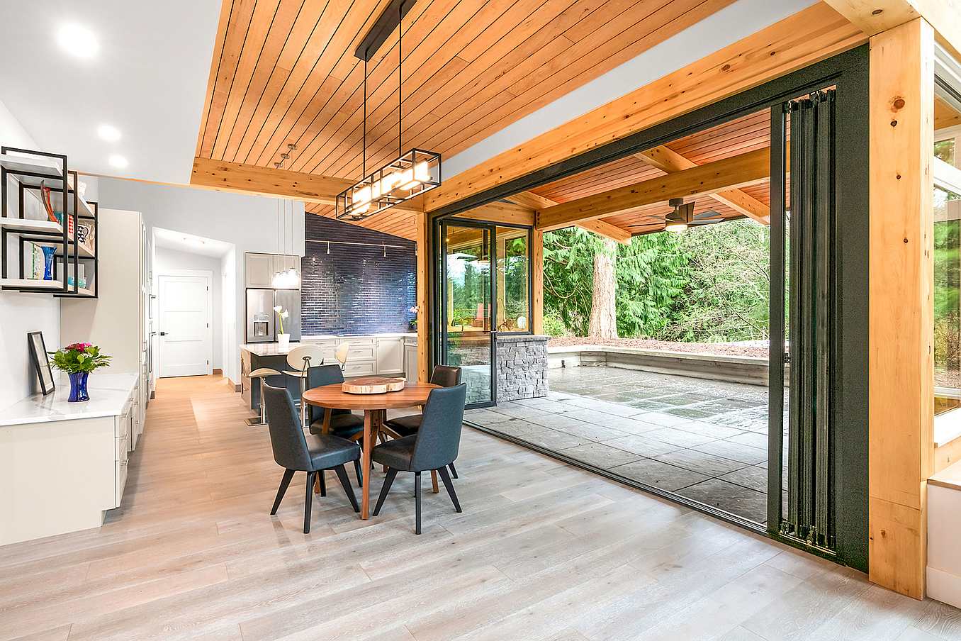 Spacious open-plan room with a dining area and bifold glass doors leading to a covered patio and tree view. 