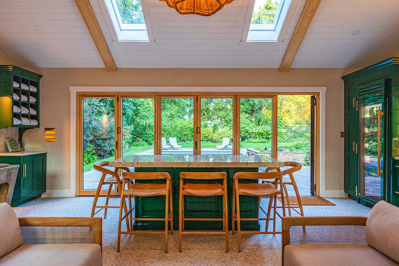 Interior view of a modern kitchen featuring wood-framed folding glass doors with a swing door open, leading to a backyard with a pool.