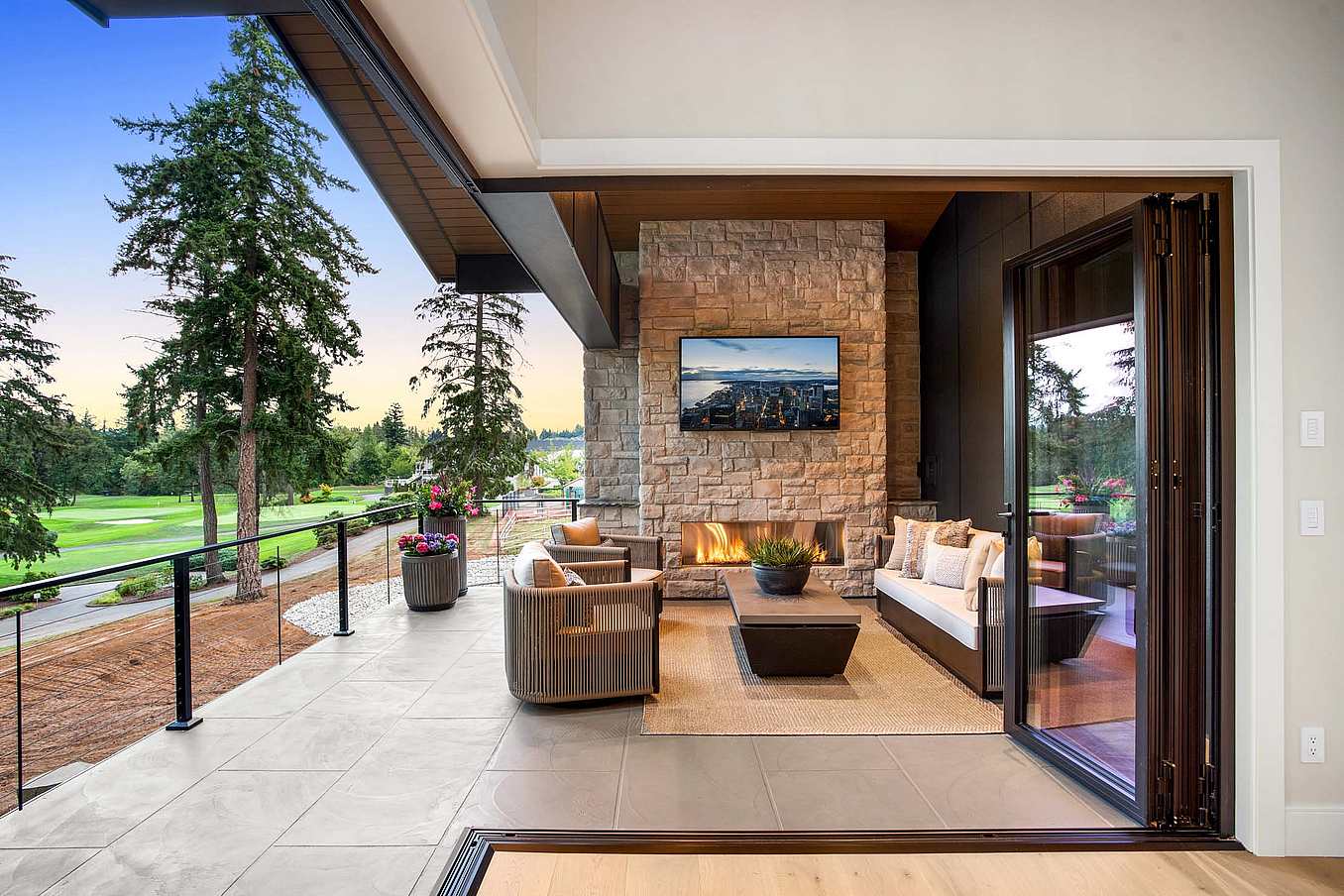 Interior view of dining room with fully open corner bifold glass doors, creating a seamless transition to the outdoor patio and golf course