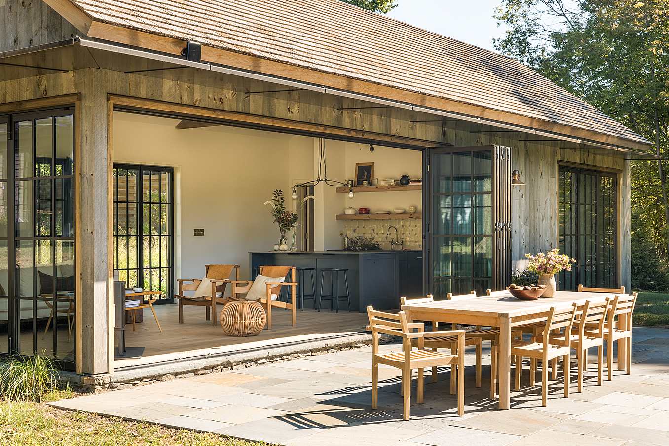 Rustic ADU exterior with folding patio glass doors folded open to outdoor terrace, showcasing seamless indoor‑outdoor living and natural wood detailing