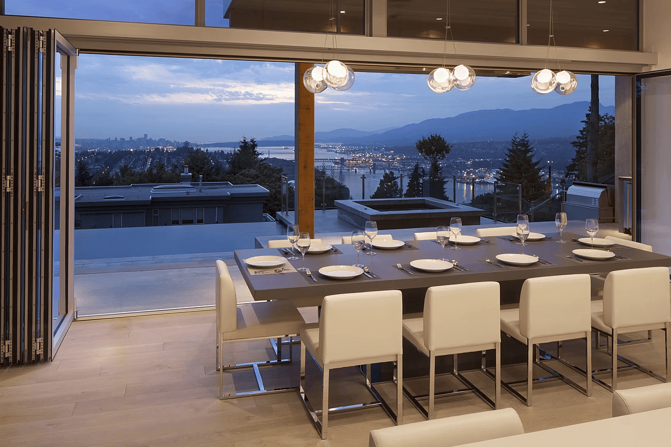 Modern dining room with intelligent rollers on folding glass doors, a table for eight, and scenic city-mountain views at dusk.