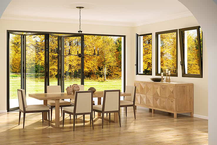 A dining room with tilt turn windows showing autumn trees, and a sideboard with candles and decorative items.