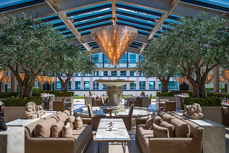 Restoration Hardware rooftop restaurant in Raleigh NC featuring outdoor dining area with sofas and tables around a central fountain under a glass roof with chandeliers and NanaWall SL70 bifold glass doors connecting indoor and outdoor spaces
