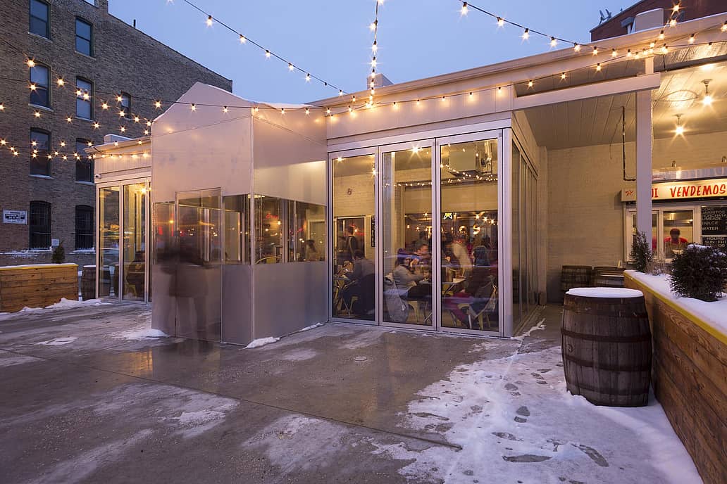 Snowy outdoor restaurant patio with String Lights featuring commercial glass doors showing indoor dining.