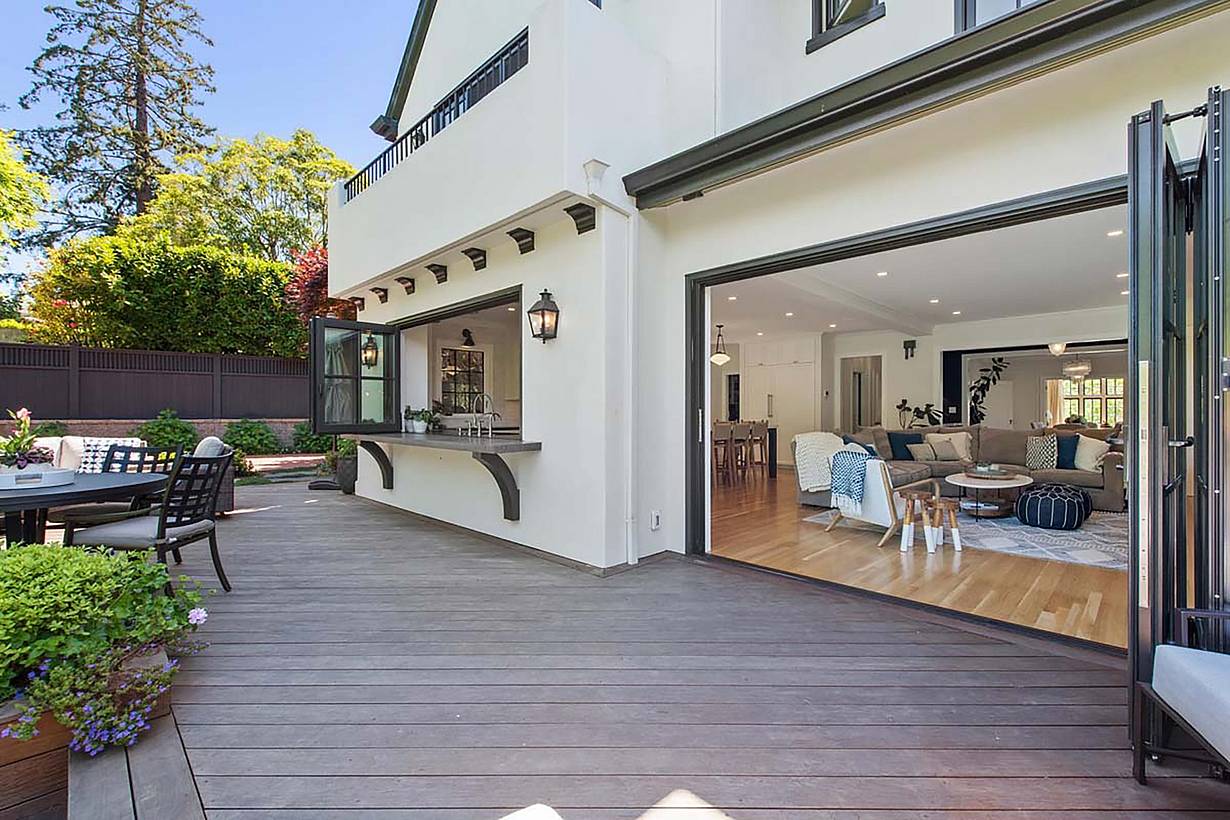 Spacious patio with wooden decking, outdoor seating, and large folding glass walls leading to a modern living room with light-colored furniture, perfectly blending style and functionality for any remodeling project.