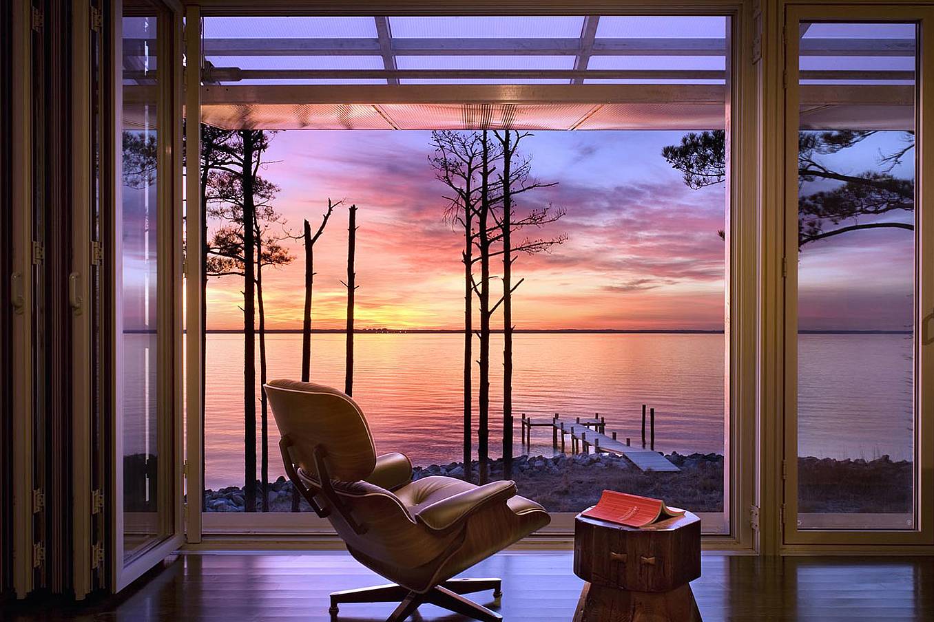 Modern living room with large glass doors opening to a lakeside view at sunset.