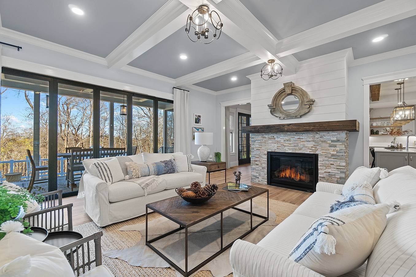 Modern Living room features white walls, a beamed ceiling, modern light fixtures, and folding glass doors that seamlessly connect indoor comfort with the natural beauty outside.