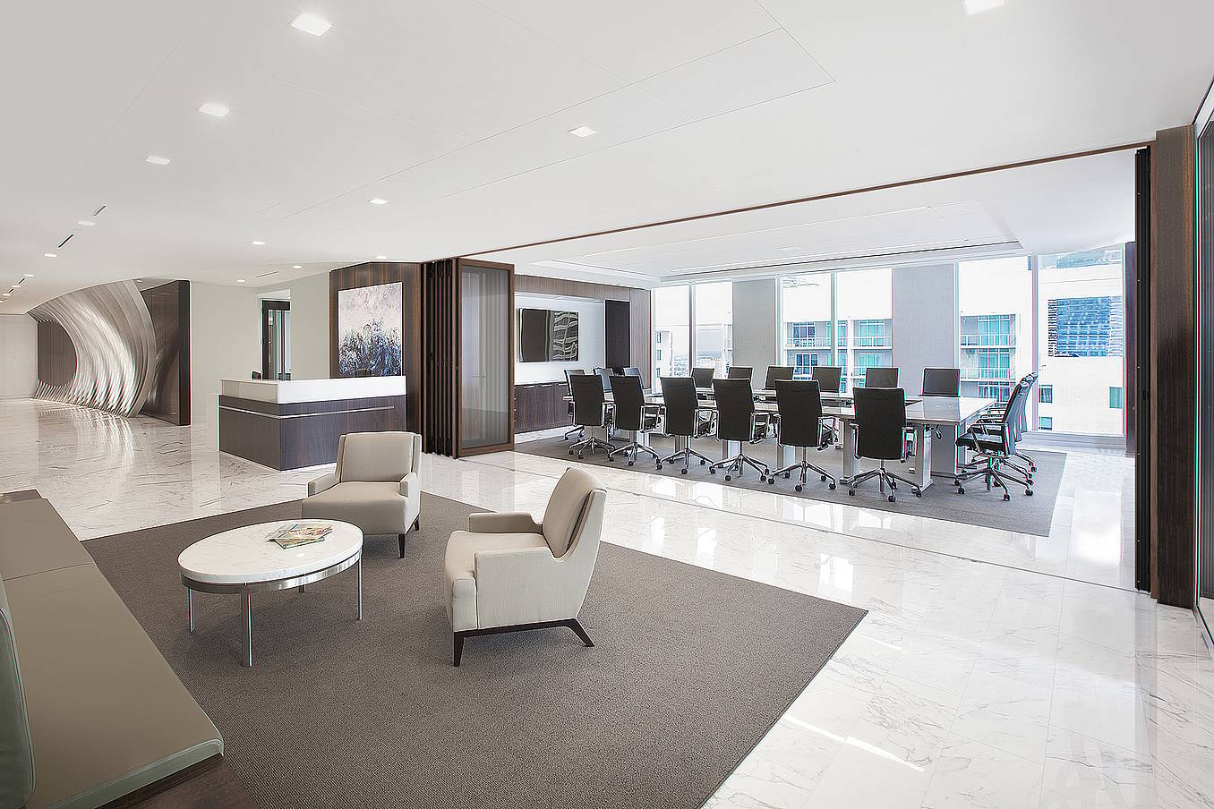 Modern office space with a reception desk, lounge area with chairs and a table, and a large glass-walled conference room.