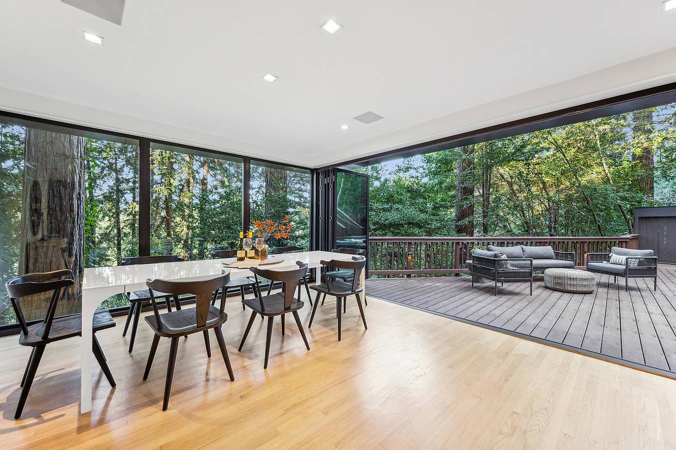 Patio glass doors in a modern dining area opening to a deck with seating and trees.