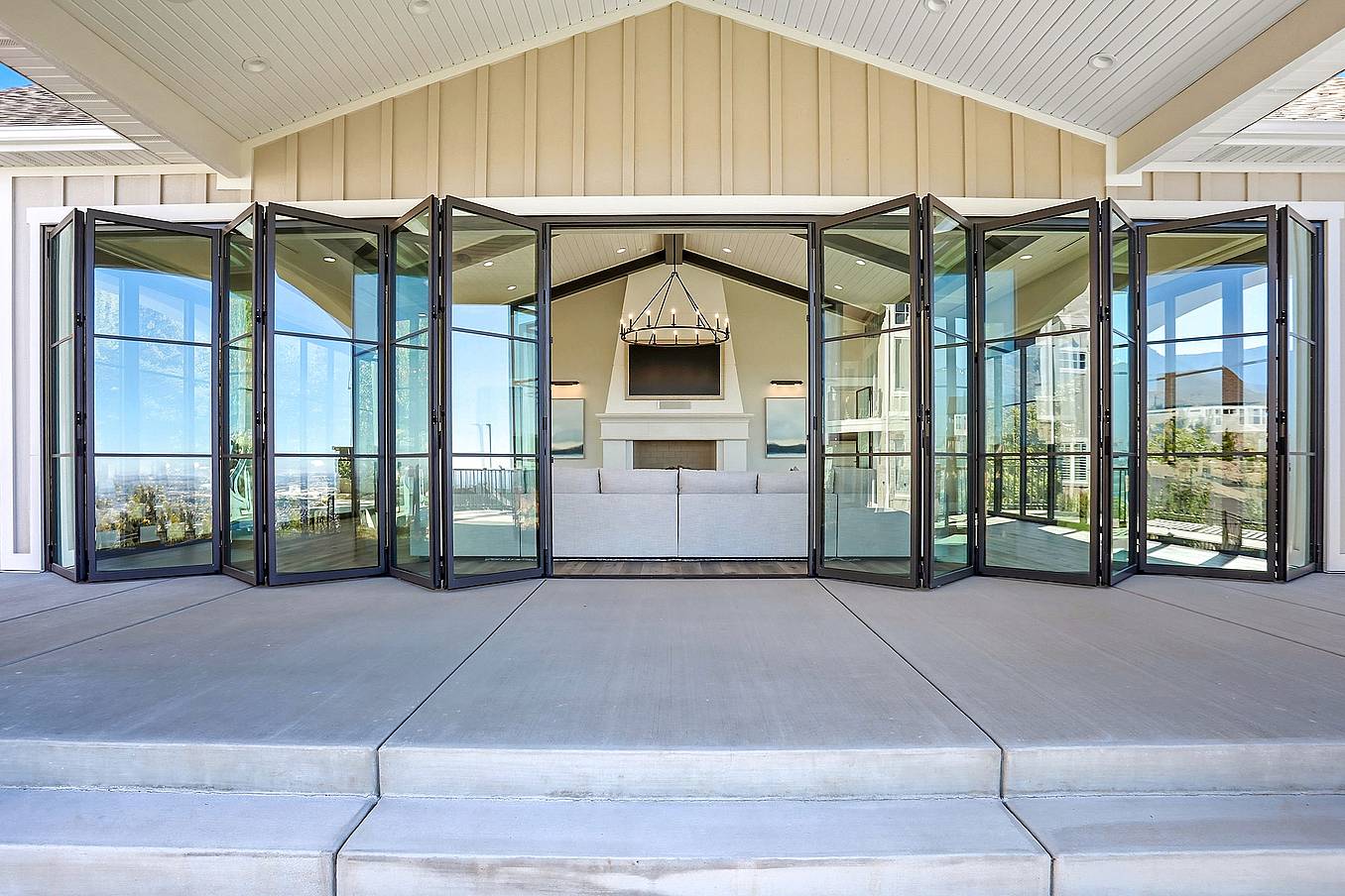Exterior white pavilion with bifold glass doors partially folded back, revealing patio seating and blending indoor-outdoor living with clean architecture