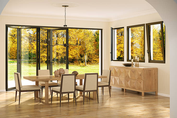 A dining room with tilt turn windows showing autumn trees, and a sideboard with candles and decorative items.